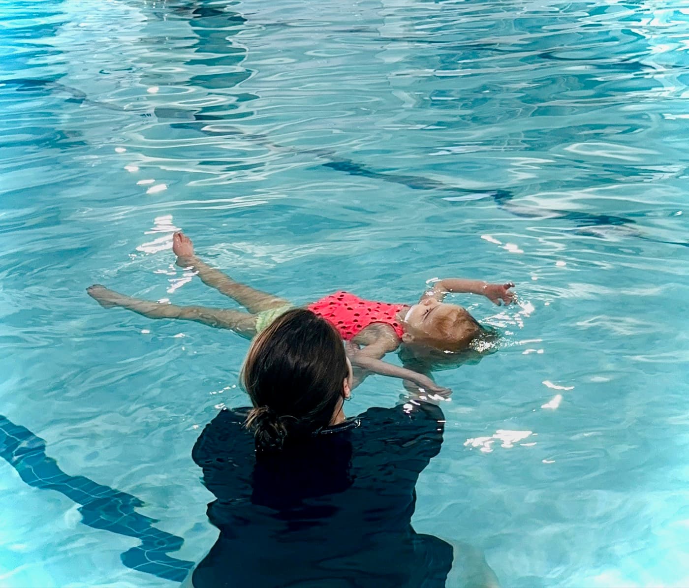 A baby practicing a survival back float, supported by the instructor