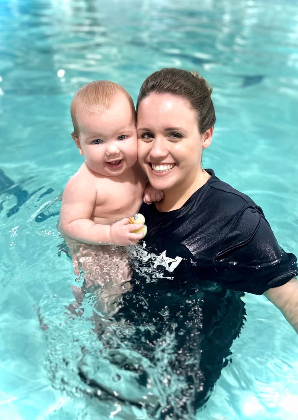 Katrina cheek-to-cheek with a smiling baby during a swim lesson