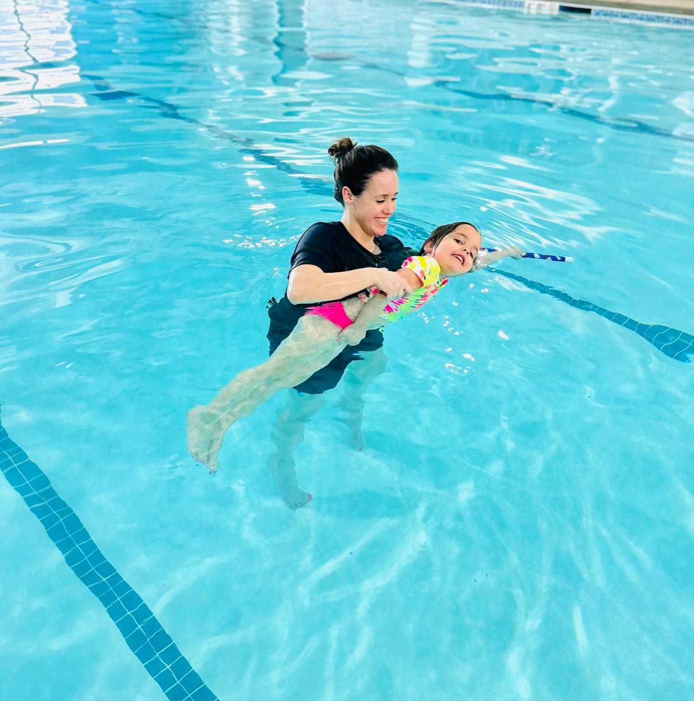 A girl practicing swimming with a kickboard alongside the instructor