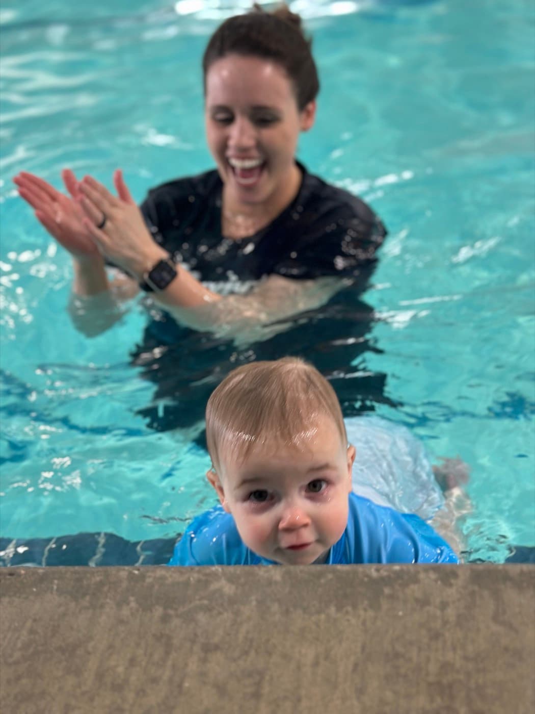 A baby reaching the pool wall while the instructor cheers